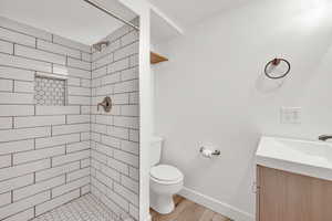 Bathroom featuring a tile shower, vanity, toilet, and wood-type flooring