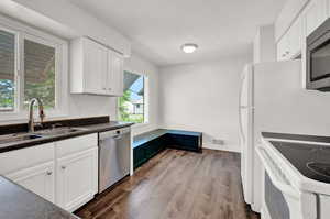 Kitchen with stainless steel appliances, hardwood / wood-style floors, white cabinetry, and sink