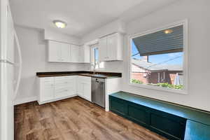 Kitchen with white cabinetry, white refrigerator, stainless steel dishwasher, hardwood / wood-style flooring, and sink