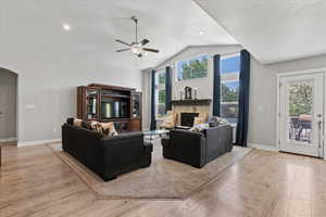 Living room with high vaulted ceiling, ceiling fan, a tile fireplace, and light wood-type flooring