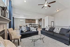 Carpeted living room with a fireplace and ceiling fan with notable chandelier