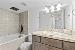 Full bathroom with vanity with extensive cabinet space, toilet, and tiled shower / bath