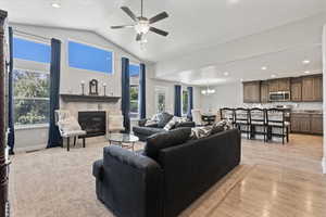 Living room with light wood-type flooring, a tiled fireplace, lofted ceiling, and ceiling fan with notable chandelier