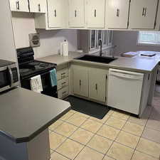 Kitchen with kitchen peninsula, white dishwasher, sink, electric stove, and light tile floors