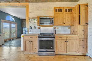 Kitchen with light brown cabinets, appliances with stainless steel finishes, tasteful backsplash, and light wood-type flooring