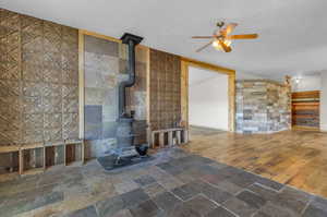 Unfurnished living room featuring dark tile flooring, ceiling fan, a wood stove, and tile walls