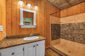 Bathroom featuring a tile shower, tile flooring, wooden walls, and vanity