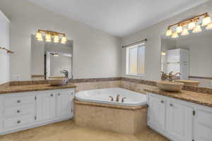 Bathroom featuring dual vanity, tiled tub, ceiling fan, and tile floors