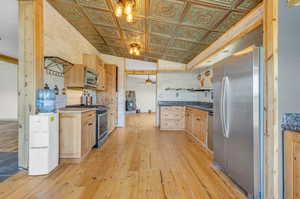 Kitchen featuring light hardwood / wood-style floors, lofted ceiling, ceiling fan with notable chandelier, stainless steel appliances, and light brown cabinetry