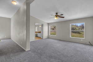 Carpeted empty room with a textured ceiling, lofted ceiling, and ceiling fan