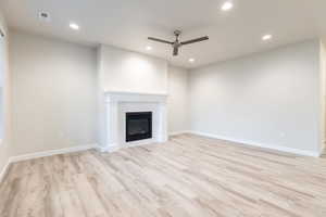 Unfurnished living room with a brick fireplace, ceiling fan, and light wood-type flooring