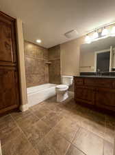 Full bathroom with tiled shower / bath combo, a textured ceiling, built in linen closet, tile floors, toilet, and vanity