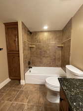 Full bathroom featuring toilet, tiled shower / bath combo, built in linen closet, tile flooring, vanity, and a textured ceiling