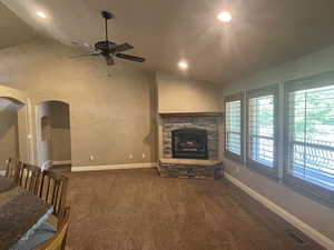 Family room with vaulted ceiling, dark colored carpet, ceiling fan, and a fireplace