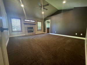 Primary bedroom featuring ceiling fan, a tiled fireplace, dark carpet, and high vaulted ceiling