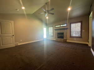 Primary bedroom featuring a tiled fireplace, ceiling fan, vaulted ceiling, and dark carpet with access to covered deck