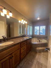 Primary bathroom featuring vanity with extensive cabinet space, tile flooring, tiled bath, double sink, and a textured ceiling