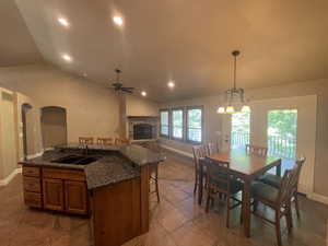 Kitchen featuring vaulted ceiling, sink, a stone fireplace, and light tile floors