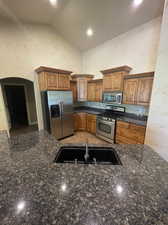 Kitchen featuring stainless steel appliances, sink, dark stone counters, and tile floors