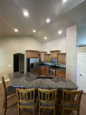 Kitchen featuring stainless steel appliances, a kitchen island with sink, a breakfast bar, and vaulted ceiling