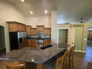 Kitchen featuring tile flooring, a breakfast bar area, sink, granite countertops, vaulted ceiling, and appliances with stainless steel finishes