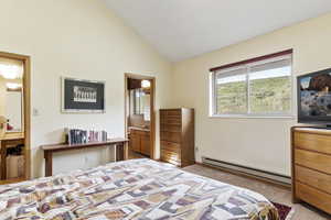 Carpeted bedroom with high vaulted ceiling, a baseboard radiator, and connected bathroom