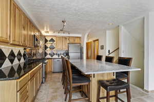 Kitchen featuring a kitchen island, backsplash, rail lighting, a kitchen bar, and appliances with stainless steel finishes