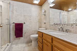 Bathroom featuring tile flooring, wooden ceiling, tile walls, large vanity, and toilet