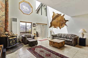 Living room featuring a high ceiling, tile floors, a wood stove, and a textured ceiling