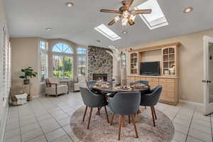 Dining room with vaulted ceiling with skylight, a fireplace, ceiling fan, and light tile floors