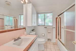 Full bathroom with a healthy amount of sunlight, shower / bath combination with glass door, toilet, and vanity with extensive cabinet space