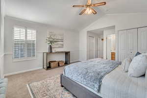 Owner's Suite - Carpeted bedroom featuring vaulted ceiling, ceiling fan, two closets, ornamental molding, and ensuite bath