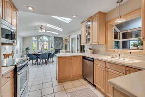 Kitchen with light brown cabinetry, kitchen peninsula, stainless steel appliances, ceiling fan, and lofted ceiling with skylight