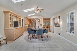 Dining room with vaulted ceiling with skylight, ceiling fan, and light tile floors