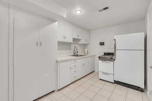 Kitchen with white appliances, white cabinets, backsplash, sink, and light tile floors