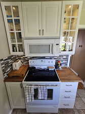 Kitchen with tasteful backsplash, butcher block countertops, tile flooring, white cabinetry, and white appliances