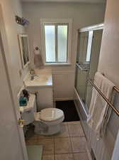 Full bathroom featuring tile floors, vanity with extensive cabinet space, combined bath / shower with glass door, and toilet