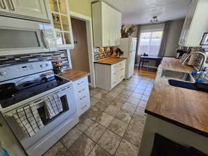 Kitchen with white cabinetry, white appliances, butcher block countertops, backsplash, and sink