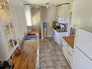 Kitchen with white appliances, tasteful backsplash, butcher block counters, sink, and white cabinets