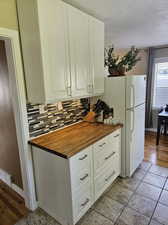 Kitchen with tasteful backsplash, butcher block counters, a textured ceiling, white cabinets, and light tile floors