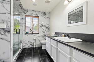 Bathroom with vanity, tile patterned floors, tile walls, an enclosed shower, and toilet