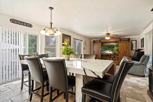 Tiled dining room featuring ceiling fan with notable chandelier and a barn door