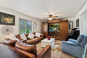 Living room with light tile patterned flooring, a textured ceiling, ceiling fan, and a barn door