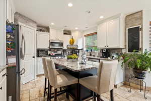 Kitchen with stainless steel appliances, white cabinets, decorative backsplash, light stone countertops, and light tile patterned flooring