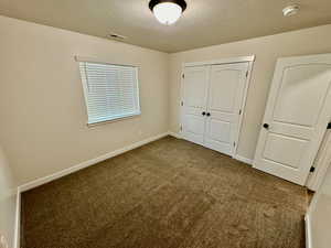 Unfurnished bedroom with a textured ceiling, a closet, and dark colored carpet