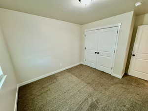 Unfurnished bedroom with a textured ceiling, a closet, and dark carpet