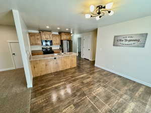 Kitchen with kitchen peninsula, a notable chandelier, black appliances, dark carpet, and sink