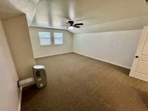 Carpeted empty room featuring ceiling fan, a textured ceiling, and lofted ceiling