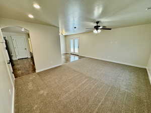 Empty room with dark carpet, ceiling fan, and a textured ceiling