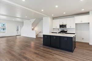 Kitchen with appliances with stainless steel finishes, white cabinetry, a center island with sink, and hardwood / wood-style floors